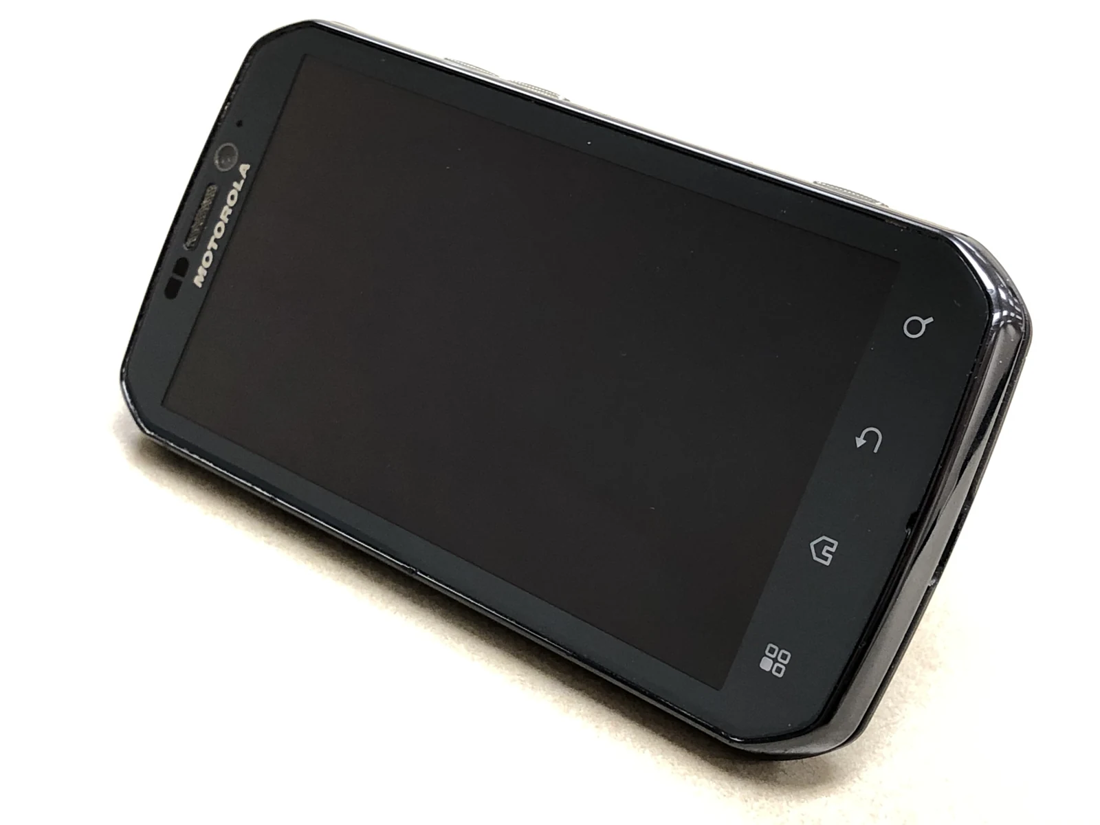 Beyaz zeminde çapraz duran, ekranı kapalı siyah Motorola telefon.
