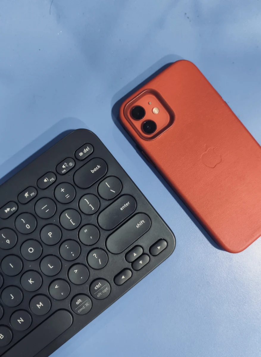 Mavi yüzeyde siyah klavyenin yanında, arka yüzü görünen kırmızı kılıflı iPhone.
