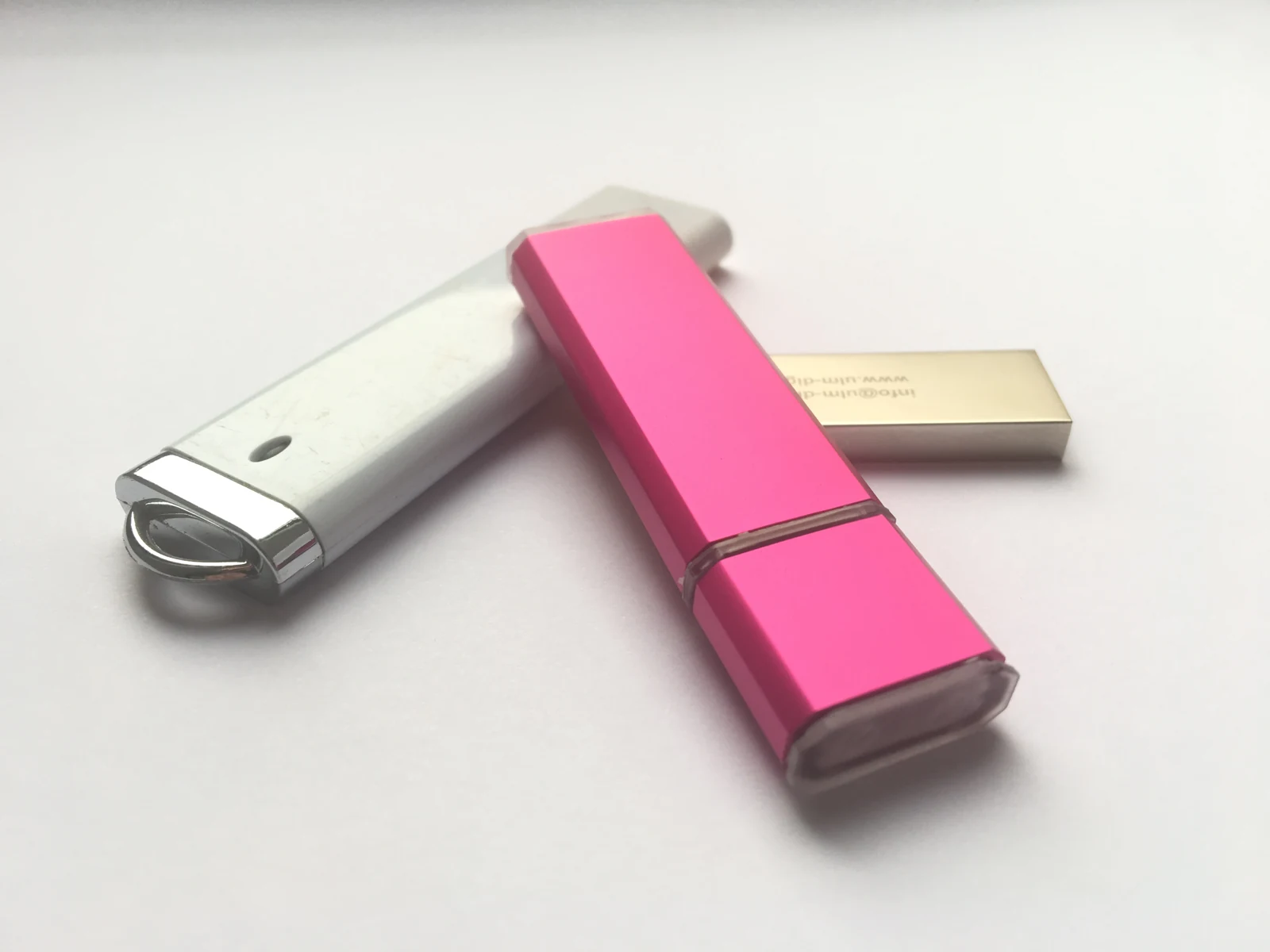 Açık renkli bir yüzeyde üst üste duran pembe, gümüş ve altın renkli üç USB bellek.